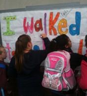 middle-school students sign their names on a wall poster that says "I walked to school"